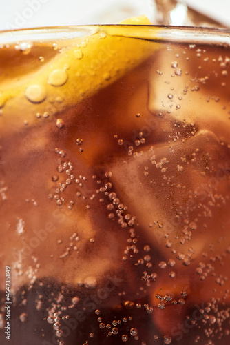 Close up shot of bubbles inside a glass of coke, sweet soda drink with ice cubes and lemon