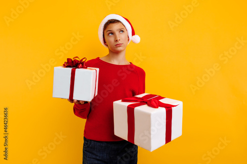 Pensive boy in a Christmas hat and a gift in his hands. Thought thinks what is inside the gifts. On a yellow background