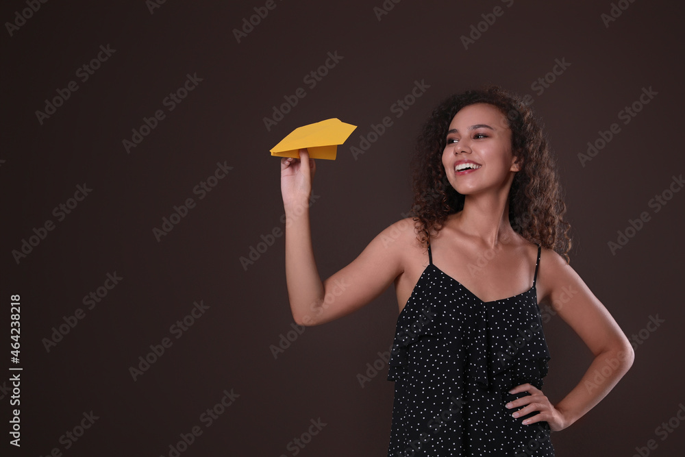 Beautiful African-American woman playing with paper plane on brown background. Space for text Beautiful African-American woman playing with paper plane on brown background. Space for text