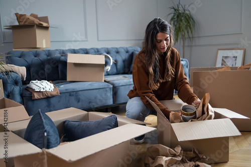 Young woman wrapping a vase while packing boxes before moving out of the apartment. photo