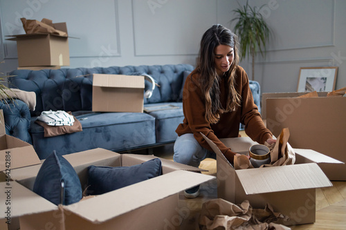 Obraz na płótnie Young woman wrapping a vase while packing boxes before moving out of the apartment. w salonie