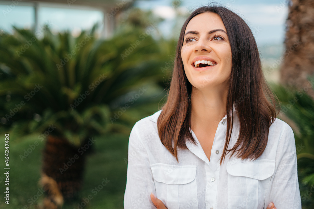 Portrait of Attractive happy i brunette woman smiling using smart phone in summer garden detailing in white shirt. The concept of communication and comfort. Portrait of Attractive happy i brunette woman smiling using smart phone in summer garden detailing in white shirt. The concept of communication and comfort.