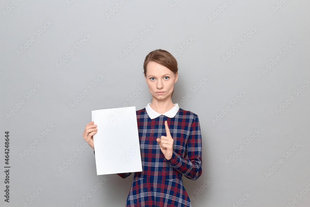 Serious young woman is holding paper sheet, raising index finger up Serious young woman is holding paper sheet, raising index finger up
