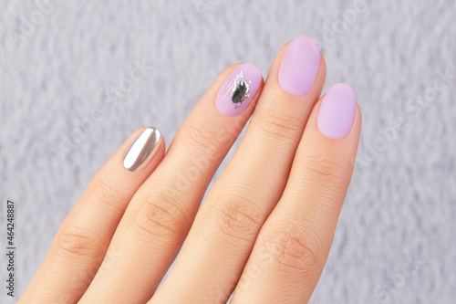 Close up womans hand with matte lavender nail design on gray furry background