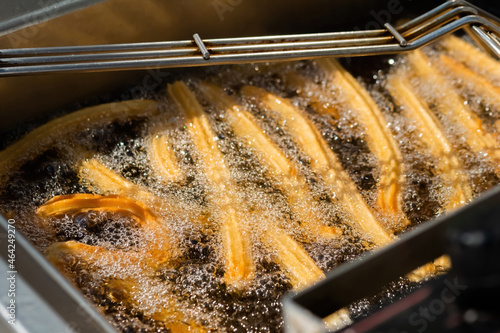 Process of cooking homemade crunchy yellow churros in boiling oil at summer outdoor food market - close up view. Traditional spanich cuisine, cookery, gastronomy, street food concept
