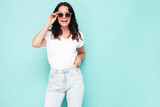 Portrait of young beautiful smiling female in trendy summer clothes. Sexy carefree woman posing near blue wall in studio. Positive model having fun indoors. Cheerful and happy. In sunglasses