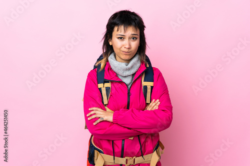 Young mountaineer girl with a big backpack over isolated pink background sad