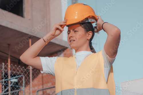 Mujer joven ingeniera retocándose el casco de seguridad para comenzar con la construcción de la estructura para la inmobiliaria junto con otros trabajadores de obra
