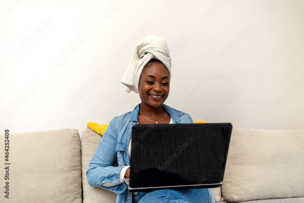 Beautiful woman after morning shower, head wrapped in towel sitting on couch in the living room taking notes by using laptop. Young woman working from her home during the quarantine due to Covid-19. Beautiful woman after morning shower, head wrapped in towel sitting on couch in the living room taking notes by using laptop. Young woman working from her home during the quarantine due to Covid-19.
