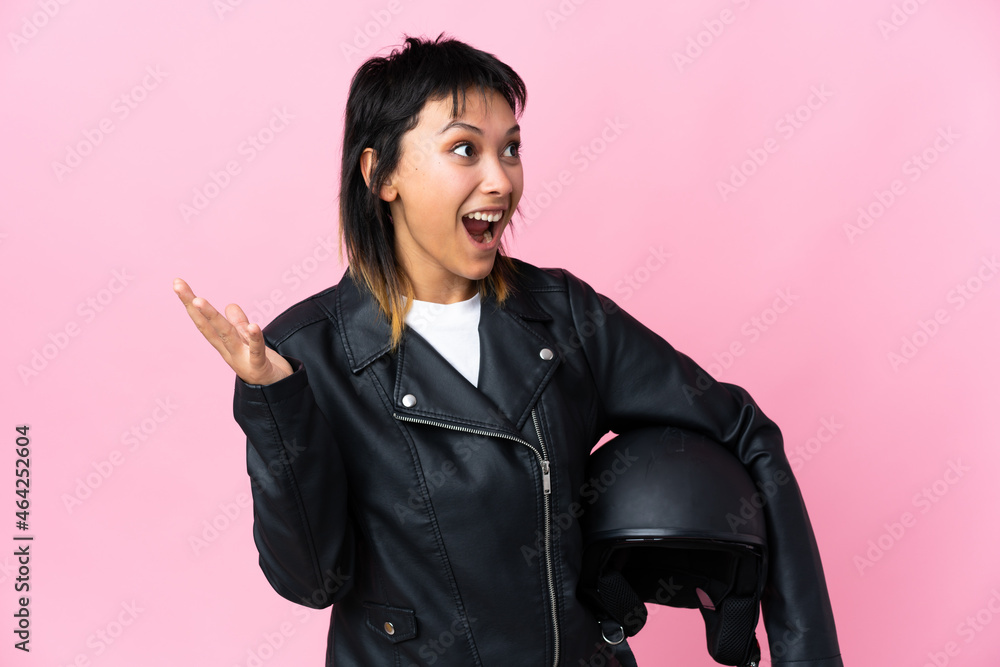 Young Uruguayan woman holding a motorcycle helmet over isolated pink background with surprise facial expression Young Uruguayan woman holding a motorcycle helmet over isolated pink background with surprise facial expression