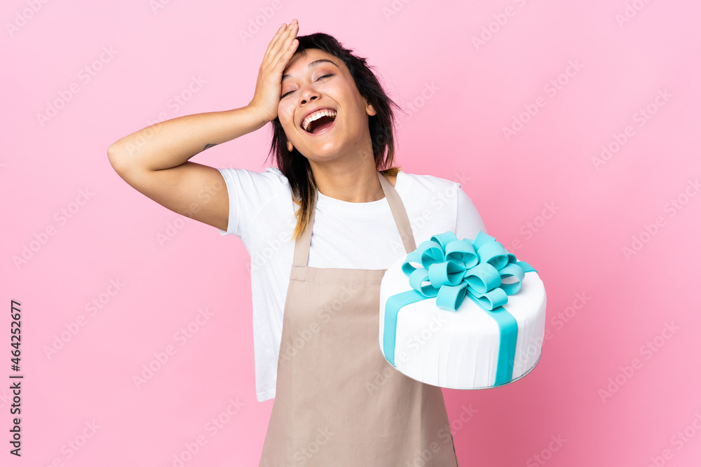Uruguayan Pastry chef holding a big cake over isolated pink background laughing Uruguayan Pastry chef holding a big cake over isolated pink background laughing
