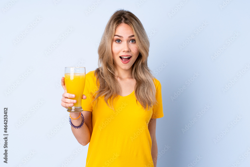 Teenager Russian girl holding an orange juice isolated on blue background with surprise and shocked facial expression Teenager Russian girl holding an orange juice isolated on blue background with surprise and shocked facial expression