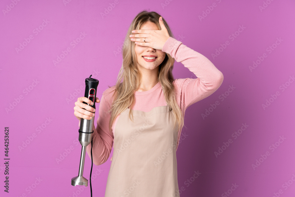 Teenager Russian girl using hand blender isolated on purple background covering eyes by hands