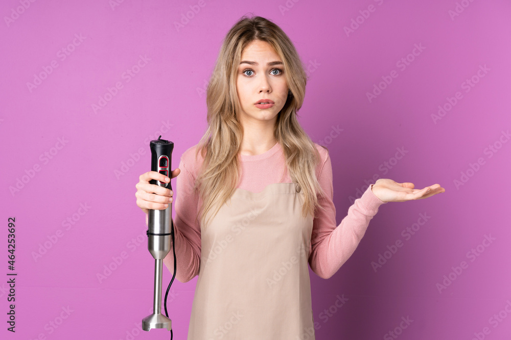 Teenager Russian girl using hand blender isolated on purple background making doubts gesture Teenager Russian girl using hand blender isolated on purple background making doubts gesture
