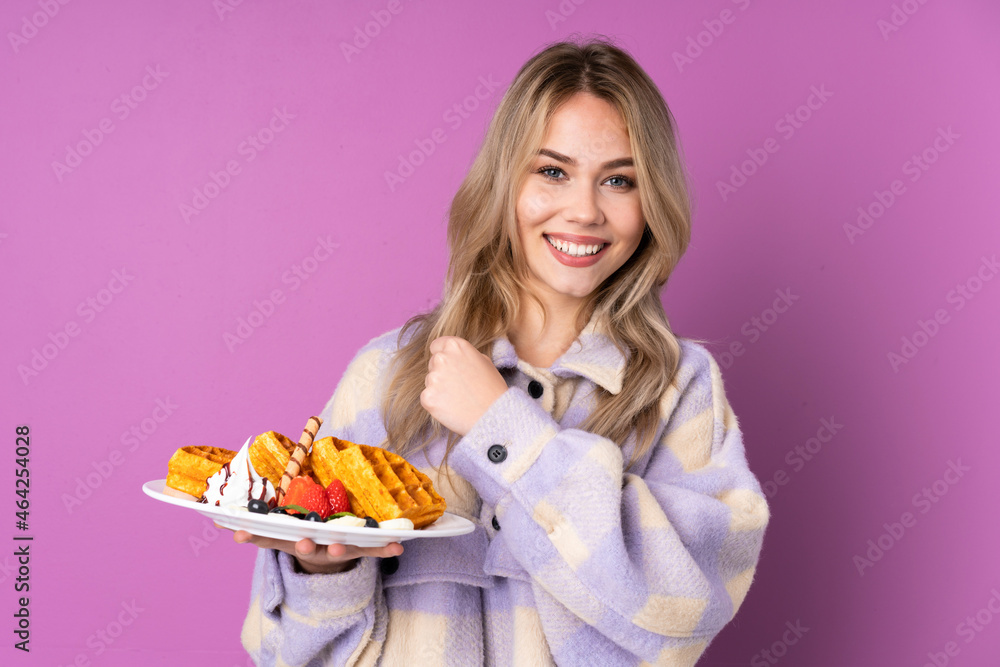 Teenager Russian girl holding waffles isolated on purple background celebrating a victory Teenager Russian girl holding waffles isolated on purple background celebrating a victory