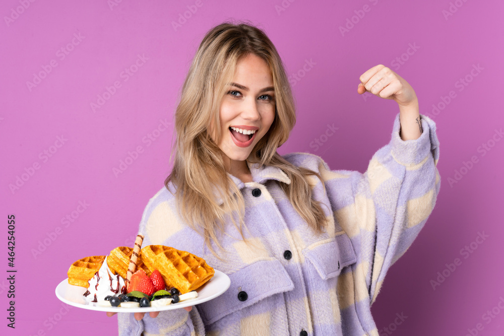 Teenager Russian girl holding waffles isolated on purple background doing strong gesture Teenager Russian girl holding waffles isolated on purple background doing strong gesture