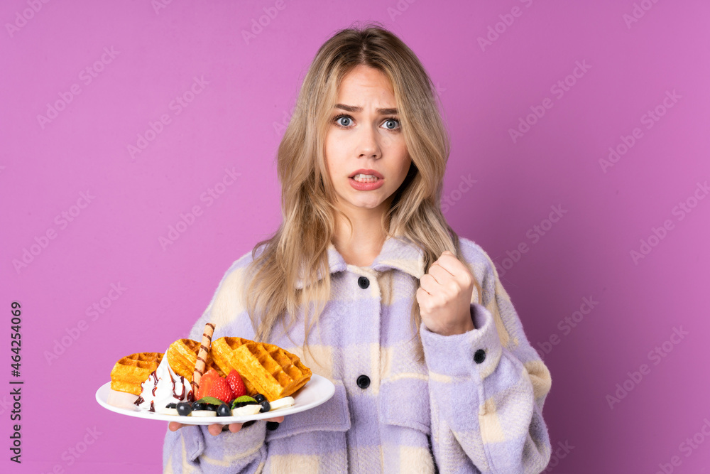 Teenager Russian girl holding waffles isolated on purple background frustrated by a bad situation