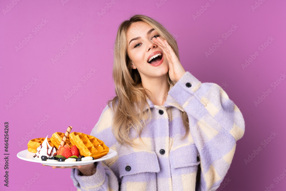 Teenager Russian girl holding waffles isolated on purple background shouting and announcing something Teenager Russian girl holding waffles isolated on purple background shouting and announcing something