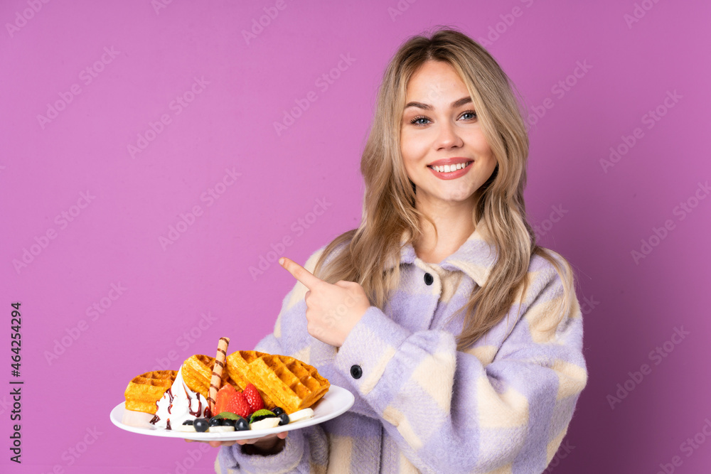 Teenager Russian girl holding waffles isolated on purple background pointing back Teenager Russian girl holding waffles isolated on purple background pointing back