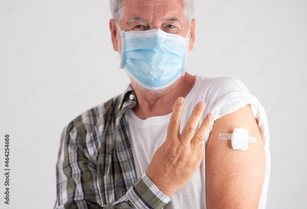 Portrait studio shot of old caucasian senior man patient wearing face mask showing with fingers number three as third doses of covid-19 coronavirus vaccine, looking at camera - obrazy, fototapety, plakaty 