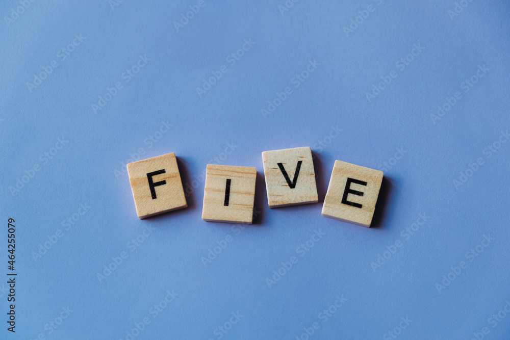 Number five laid out from tiles in words. Wooden tiles on a blue background with letters. View from above. Copy space. Number five laid out from tiles in words. Wooden tiles on a blue background with letters. View from above. Copy space.