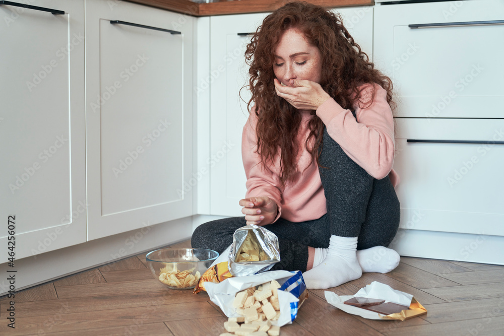 Young caucasian woman having eating disorder and eating greedily on the floor - obrazy, fototapety, plakaty 