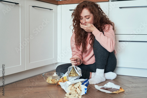 Young caucasian woman having eating disorder and eating greedily on the floor Poster Mural XXL