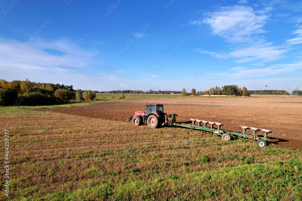 Obraz premium Tractor with Plough on Plowed. Ploughing and Soil Tillage. Agricultural Tractor on Cultivation Field for Sowing Seeds. Tractor During Field Cultivating. Planting and Seeding Equipment.