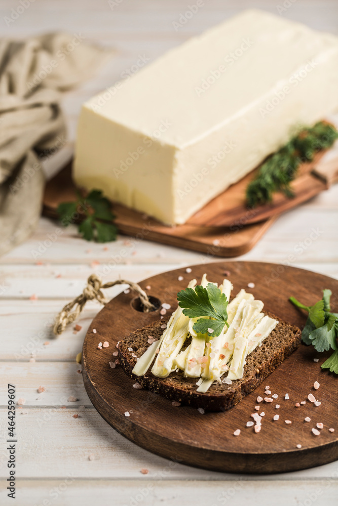 Soft and fresh butter slices spread on black bread with fresh herbs on a wooden board. Soft and fresh butter slices spread on black bread with fresh herbs on a wooden board.