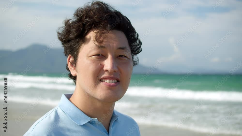 Portrait of a middle-aged asian man in a blue shirt standing on the beach by the sea against the backdrop of high mountains Portrait of a middle-aged asian man in a blue shirt standing on the beach by the sea against the backdrop of high mountains