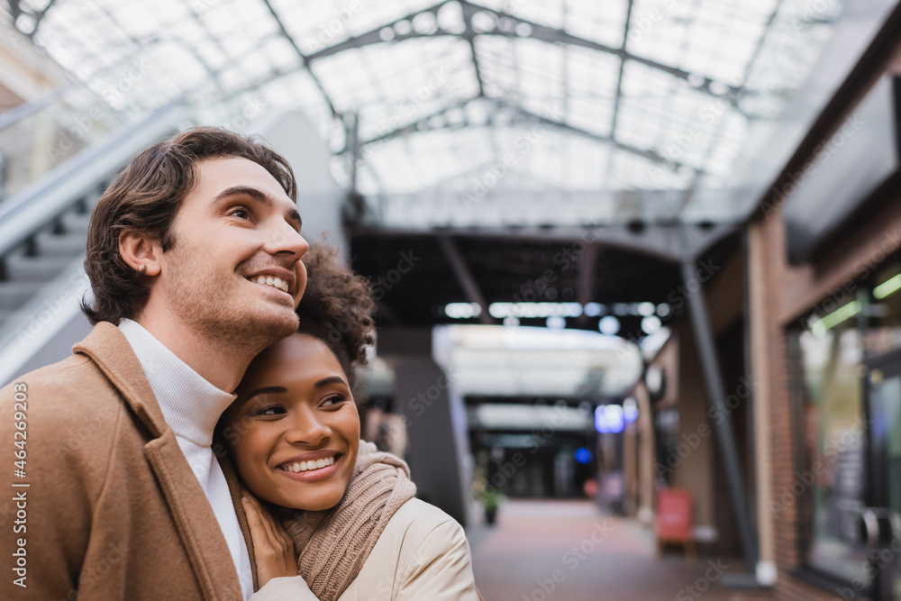pleased interracial couple smiling in shopping mall. pleased interracial couple smiling in shopping mall.