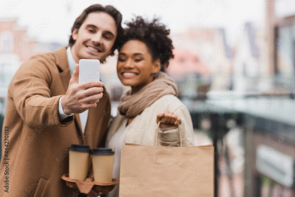 blurred multiethnic couple with paper cups and shopping bag taking selfie in mall. blurred multiethnic couple with paper cups and shopping bag taking selfie in mall.