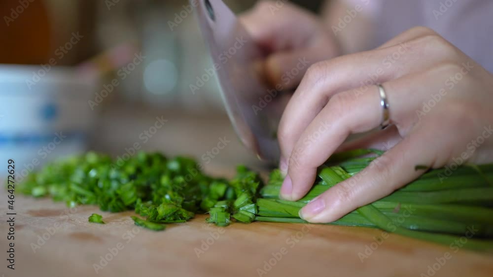 Woman chopping green onion on wooden board in kitchen Woman chopping green onion on wooden board in kitchen