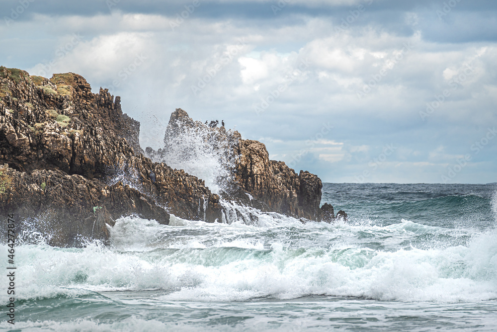 Rock Formations On Beach Against Sky. Beautiful ocean beach with large rocks on the shore and in the water. Powerful waves on ocean. Ocean water splash on rock beach with Rugged cliffs