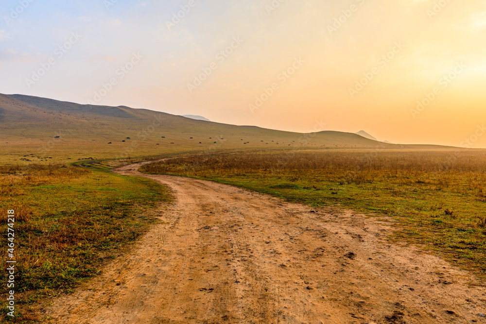 Country dirt road and mountain landscape at sunrise.