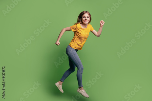 Portrait of charming sporty positive lady jump run wear yellow t-shirt jeans footwear on green background