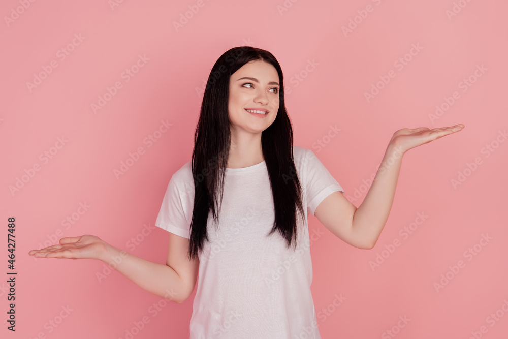 Photo of funny dreamy lady palms weighing empty space object isolated on pink color background Photo of funny dreamy lady palms weighing empty space object isolated on pink color background