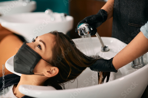 Smiling woman with face mask enjoys while washing hair at hairdresser's.