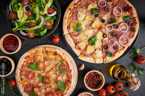 assorted foodset on table. Italian pizza and pizza cooking ingredients on dark stone background. tomatoes on vine, mozzarella, black olives, herbs and spices, vegetable salad. top view.