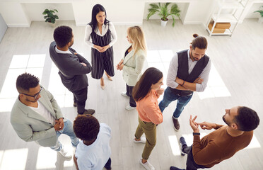 Groups of multi ethnic people standing in office and talking. Diverse men and women communicating during casual corporate meeting, psychological training or after business event. High angle shot