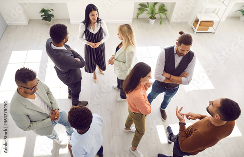 Groups of multi ethnic people standing in office and talking. Diverse men and women communicating during casual corporate meeting, psychological training or after business event. High angle shot photo