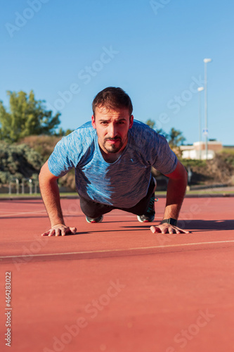 Vertical image of an adult man doing pushup looking at camera.Hard training outdoors with effort, sport, fitness and health concept. © Dani D.G