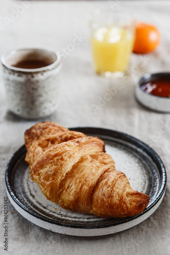 Breakfast with croissant, jam and hot chocolate, juice and tangerine on greige linen tablecloth. Selective focus