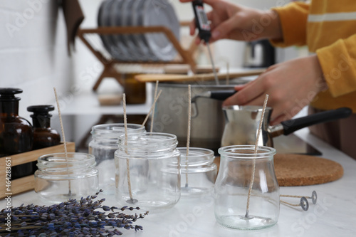 Woman making aromatic candles at white table indoors  focus on empty jars