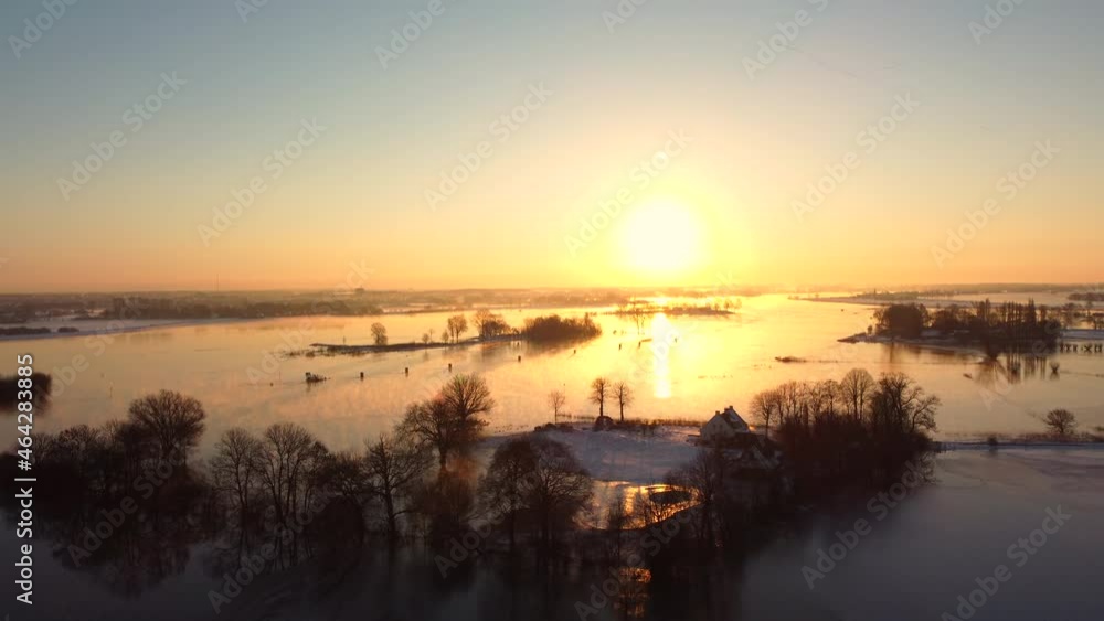 Foggy winter sunrise over the river IJssel with a high water level and ice and snow during a cold day in The Netherlands. Aerial drone point of view. Foggy winter sunrise over the river IJssel with a high water level and ice and snow during a cold day in The Netherlands. Aerial drone point of view.
