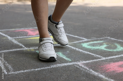 Little child playing hopscotch drawn with chalk on asphalt outdoors, closeup