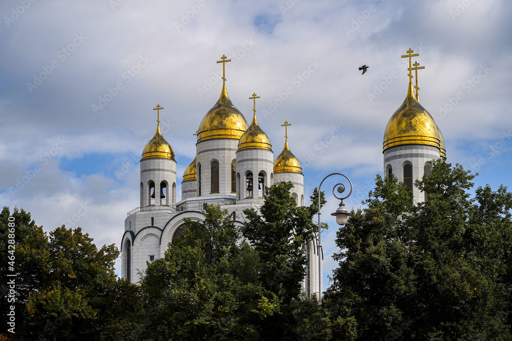 Golden domes of the church sparkle against the background of a blue sky and clouds