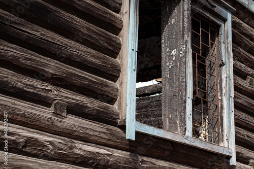The wall of a burnt log house with a broken window, close-up.