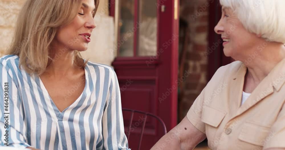 Cute gray-haired woman sitting at restaurant table with her daughter and talking about life spending the weekend together. Cute gray-haired woman sitting at restaurant table with her daughter and talking about life spending the weekend together.
