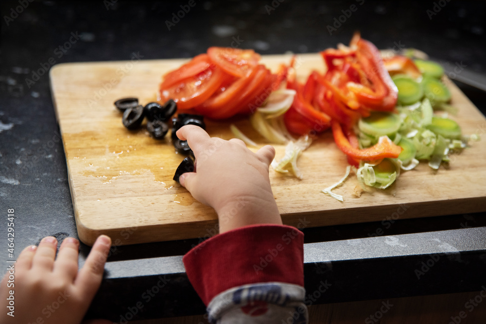Obraz na płótnie Rączka dziecka sięga po oliwkę na desce z pokrojonymi warzywami w salonie
